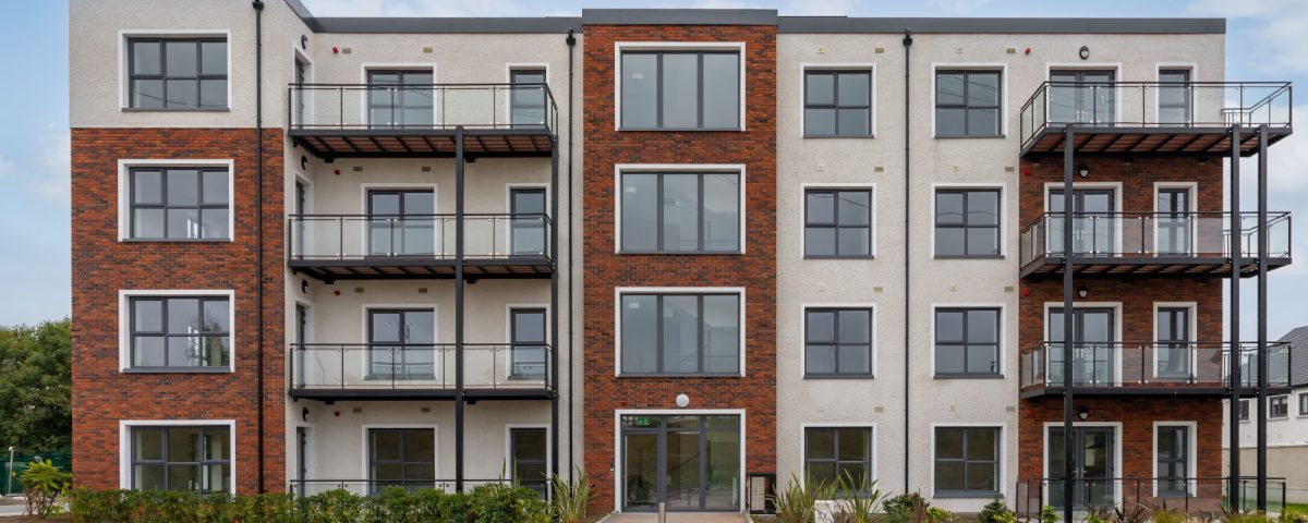 A large multi-story apartment building. There is a series of balconies made from glass railings with large windows behind them.